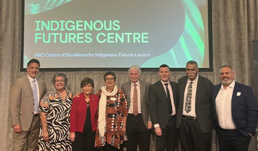 A group of men and women stand side by side on stage with a slide behind them reading Indigenous Futures Centre.